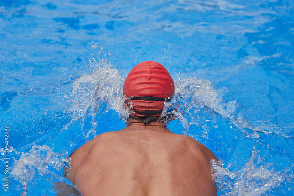 swimmer in an outdoor pool, resting on the edge of the pool with his back to the camera and entering the water
