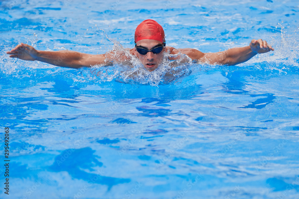 Swimmer in an outdoor pool, swimming butterfly-style, with open arms