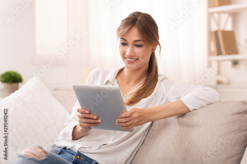 Smiling Woman Using Digital Tablet Relaxing On Sofa At Home