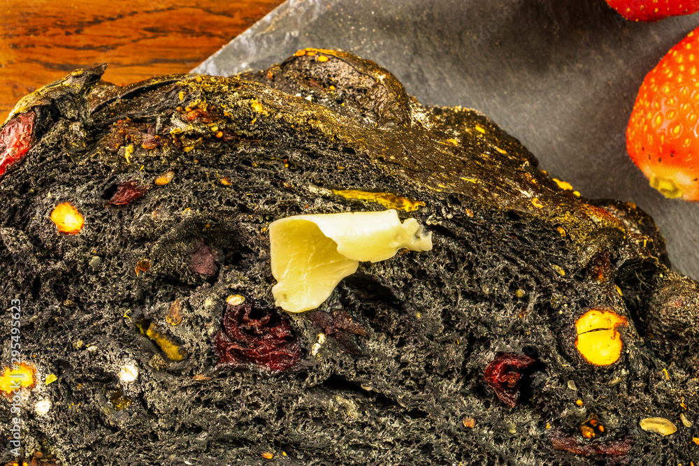 Obraz premium Détail sur une tranche de pain noir au charbon fruits secs et cranberry sur un plat en ardoise avec des fruits frais fraises et une noisette de beurre