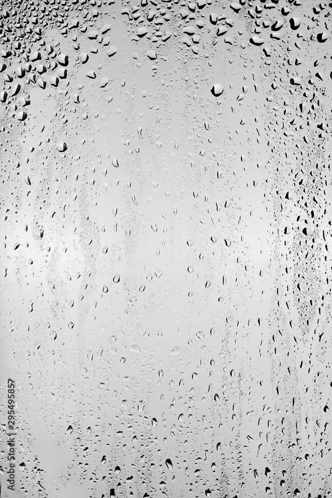 Fototapeta premium Drops of water flow down the surface of the clear glass on a gray background.