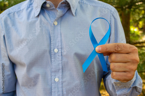 Awareness of prostate cancer, a man holding a light blue ribbon on a background of autumn leaves. To support people living with and patients . Men's health and the concept of world cancer day.