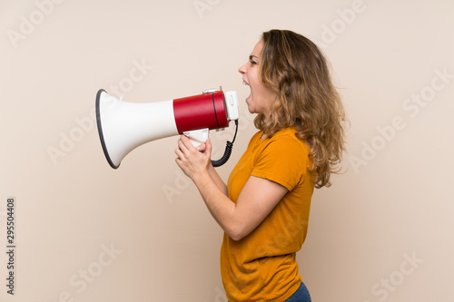 Young blonde girl over isolated background shouting through a megaphone