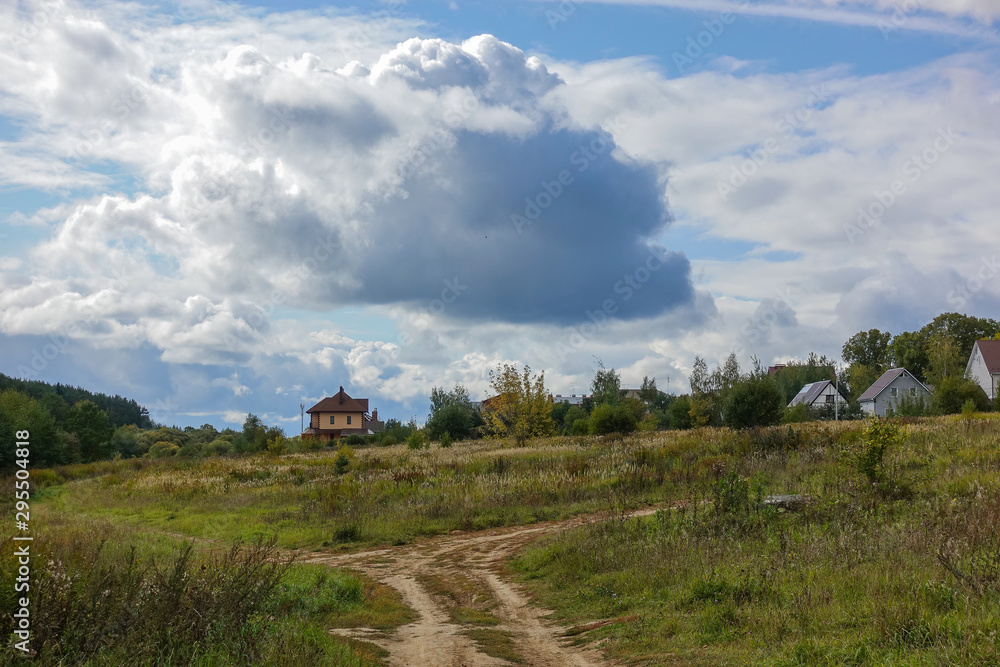 Russian rural landscape in the fall, village houses near the forest. Sky with rain clouds