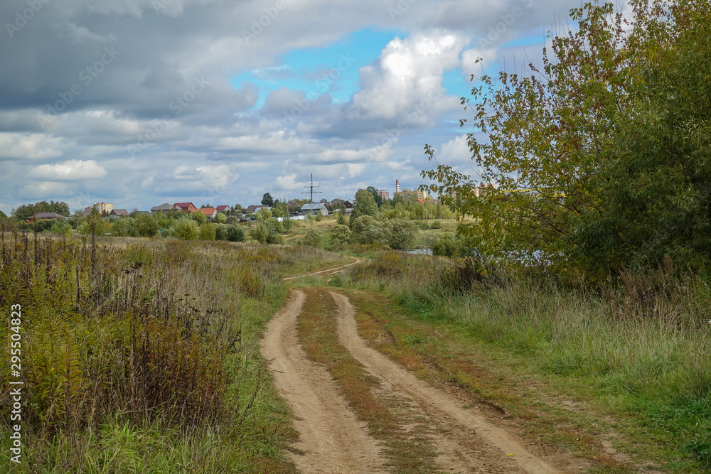 Russian rural landscape in the fall, village houses near the forest. Sky with rain clouds
