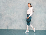 Portrait of confident fitness woman in sports clothing looking confident.Young female wearing sportswear. Beautiful model with perfect tanned body.Female walking in studio near gray wall
