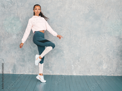 Portrait of confident fitness woman in sports clothing looking confident.Young female wearing sportswear. Beautiful model with perfect tanned body.Female jumping in studio near gray wall