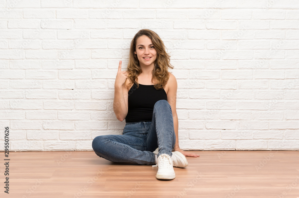 Young blonde woman sitting on the floor pointing with the index finger a great idea Young blonde woman sitting on the floor pointing with the index finger a great idea