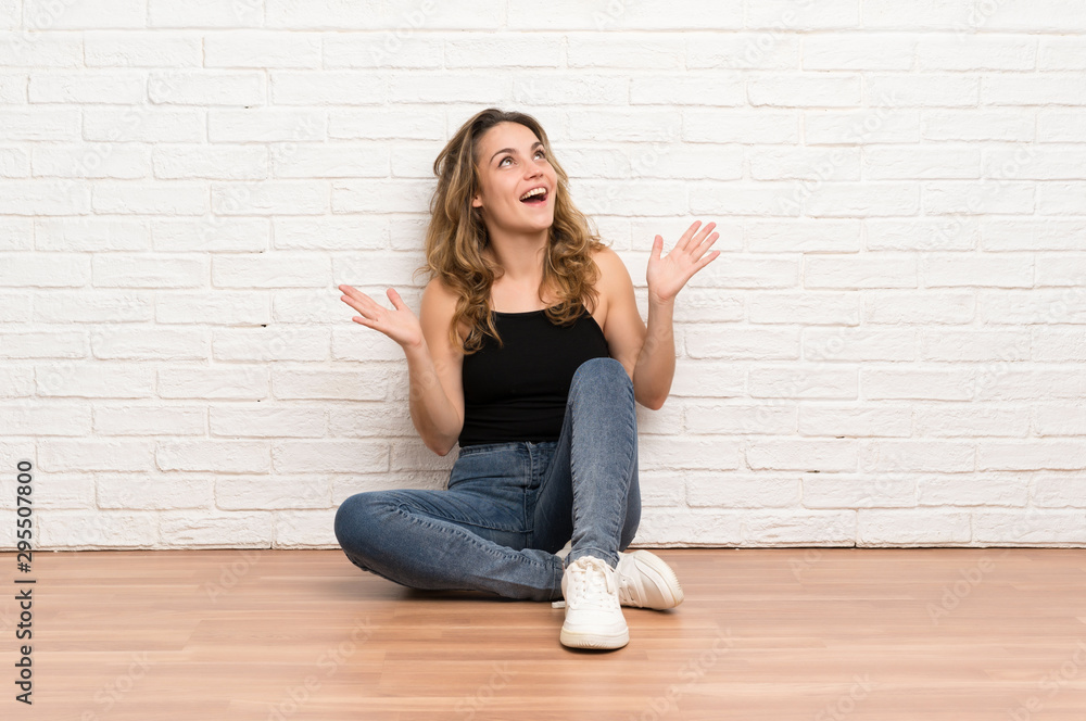 Young blonde woman sitting on the floor with surprise facial expression Young blonde woman sitting on the floor with surprise facial expression