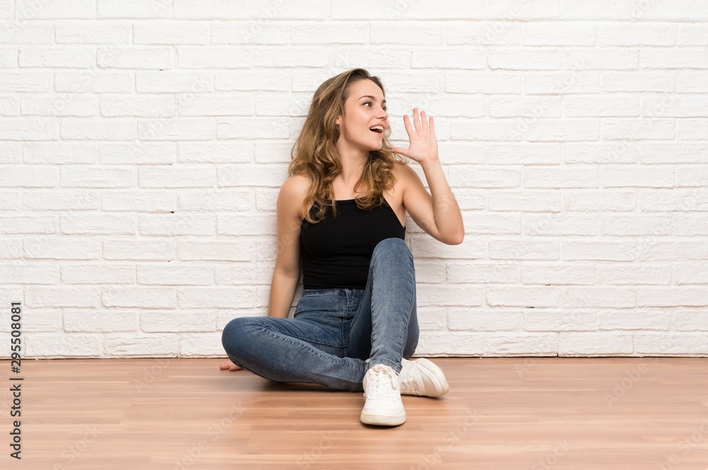 Young blonde woman sitting on the floor shouting with mouth wide open Young blonde woman sitting on the floor shouting with mouth wide open