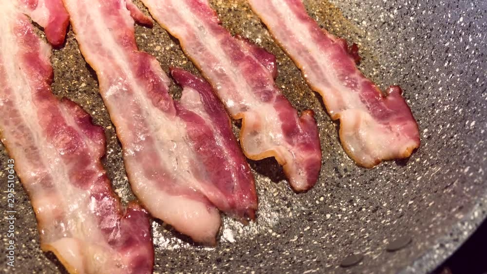 Fat fried bacon strips on the hot pan. Junk and unhealthy food concept
