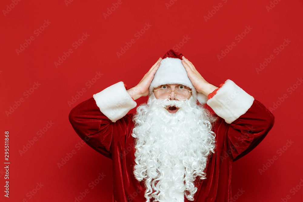 Portrait of shocked Santa Claus holding his head, looking in camera surprised at the red background. X mas.Emotional santa isolated on red background.Santa and discounts .Copyspace