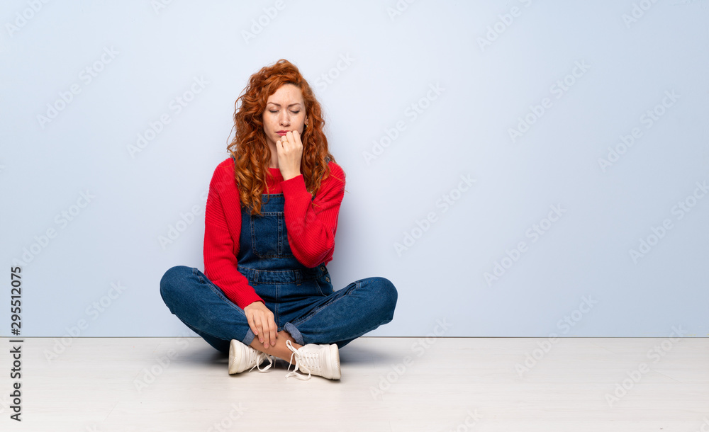 Redhead woman with overalls sitting on the floor having doubts Redhead woman with overalls sitting on the floor having doubts