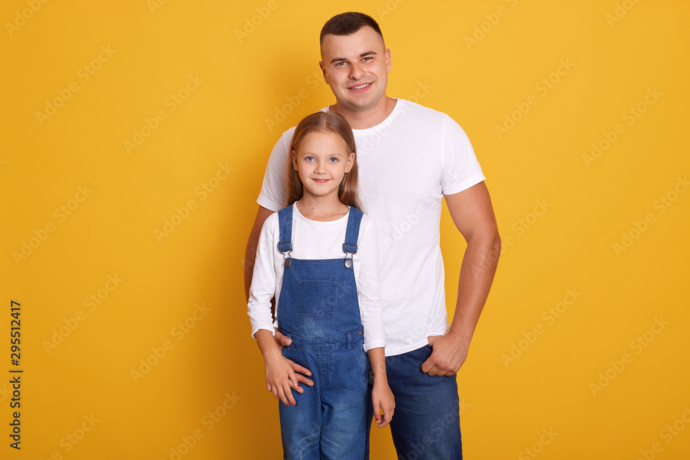 Portrait of lovely daughter smiling and standing with her handsome father isolated over yellow background, family wearing casual clothing, looking directly at camera. Deep devotion and relationship. Portrait of lovely daughter smiling and standing with her handsome father isolated over yellow background, family wearing casual clothing, looking directly at camera. Deep devotion and relationship.