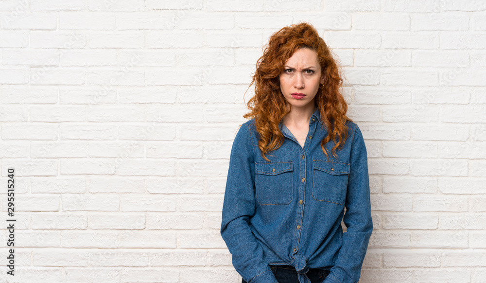 Redhead woman over white brick wall with sad and depressed expression