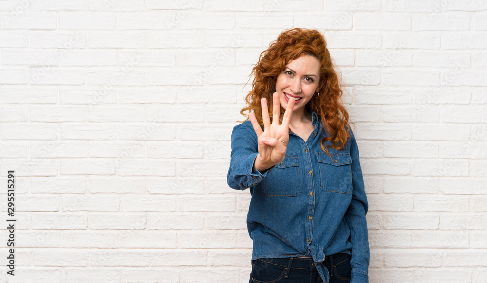 Redhead woman over white brick wall happy and counting four with fingers