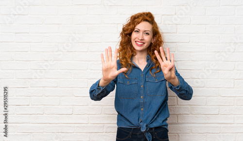 Redhead woman over white brick wall counting nine with fingers