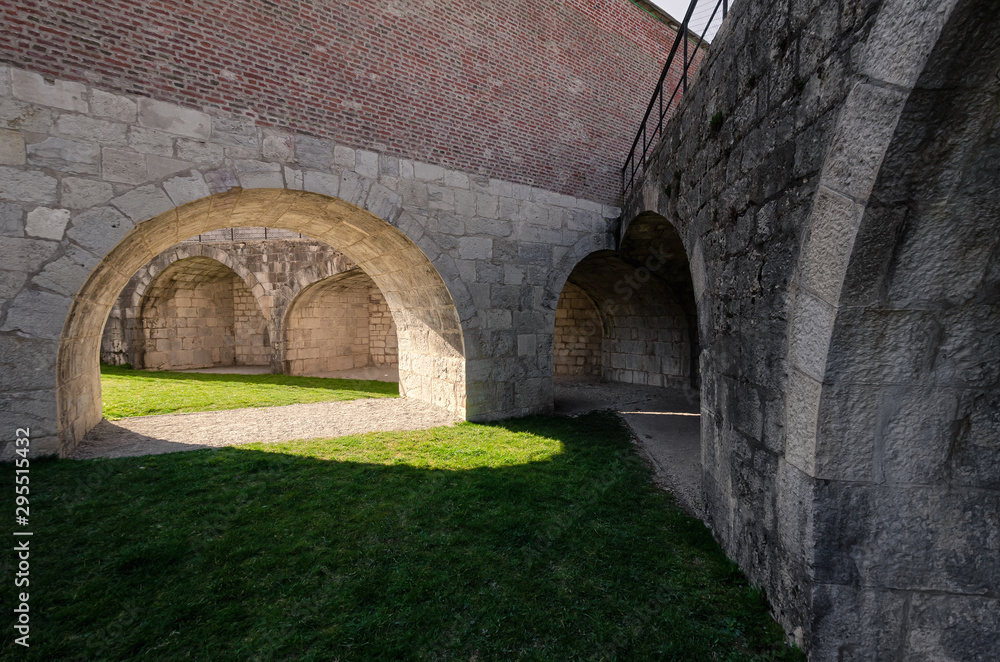 View of the courtyard of the old fortress. Skovoz an arch in a wall on a green lawn the sunlight falls. The yard is surrounded by thick stone walls. Citadel in the city of Besancon. France. Background