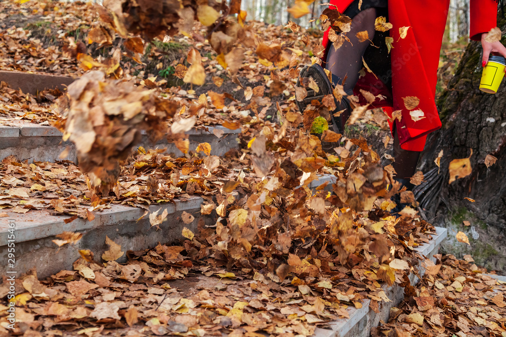 A girl in black boots and a red coat kicks yellow and red foliage strolling in the park alone on a clear autumn day during a fall. Freshness, nature and fun. A girl in black boots and a red coat kicks yellow and red foliage strolling in the park alone on a clear autumn day during a fall. Freshness, nature and fun.