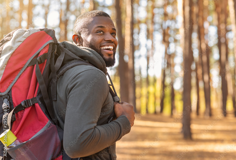 African man wearing backpack standing on forest trail - obrazy, fototapety, plakaty 