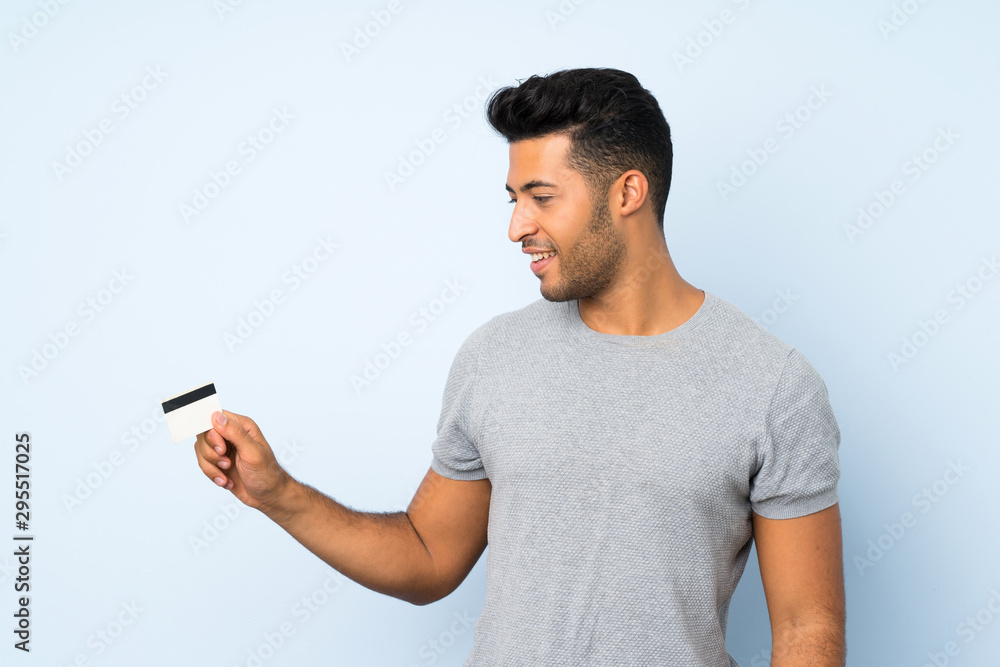 Young handsome man over isolated background holding a credit card