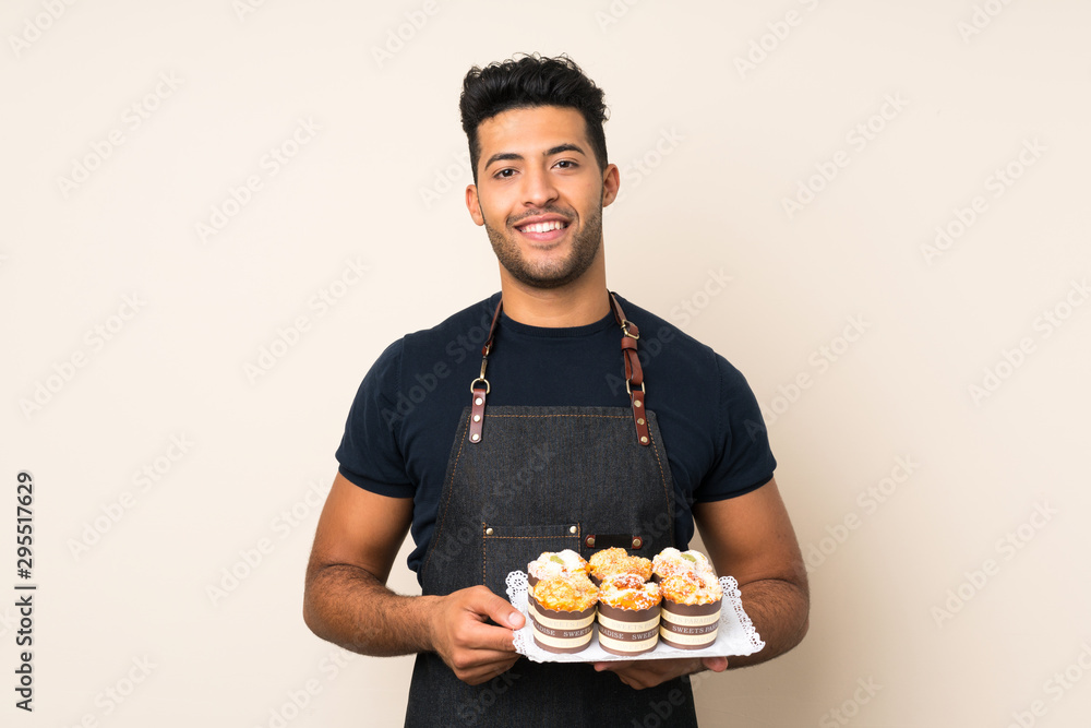 Young handsome man over isolated background holding mini cakes Young handsome man over isolated background holding mini cakes