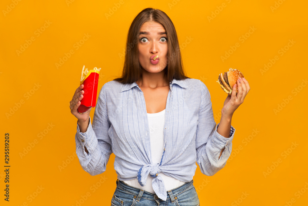 Surprised Woman Eating Burger And French Fries, Studio Shot - obrazy, fototapety, plakaty 