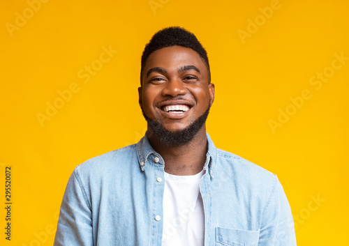 Portrait of young laughing african american guy over yellow background photo