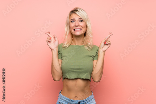 Young blonde woman over isolated pink background with fingers crossing and wishing the best