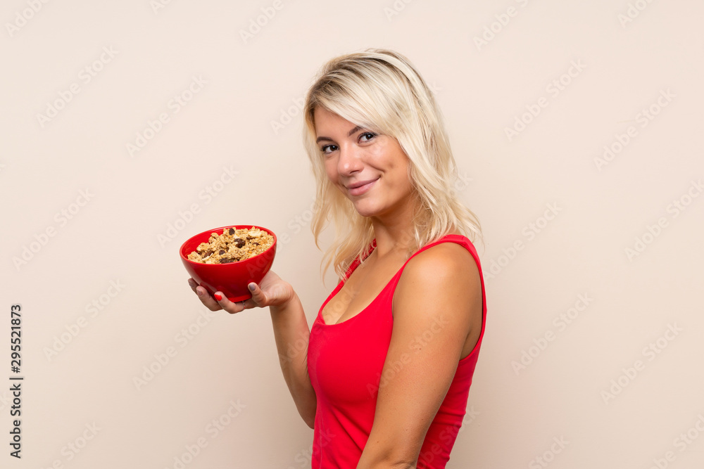 Young blonde woman over isolated background holding a bowl of cereals