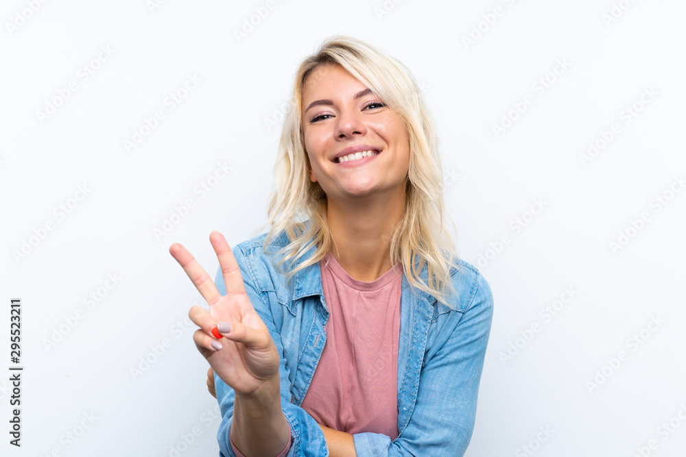 Obraz premium Young blonde woman over isolated white background smiling and showing victory sign
