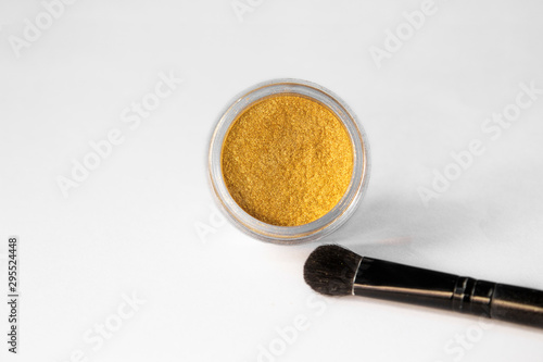 Gold eye shadows and eye brush crushed samples isolated on white background. Concept of makeup and beauty.