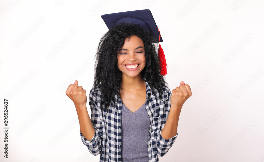 Finally! Graduate African American girl in a plaid shirt is standing and holding both of her palms in fists and smiling with her eyes closed, expressing success or victory. Finally! Graduate African American girl in a plaid shirt is standing and holding both of her palms in fists and smiling with her eyes closed, expressing success or victory.