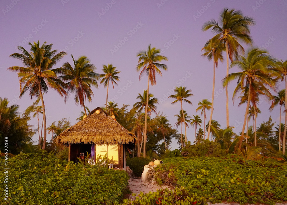 Sunrise reflects in the door of a private bungalow surrounded by palm trees on the island of Fakarava in French Polynesia