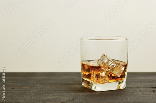 glass of whiskey with ice cubes on wooden table