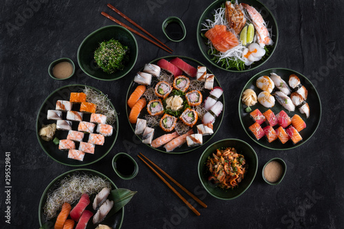 Assorted sushi set served on dark stone slate background. Top view of wakame salad, seafood,various maki rolls, sashimi and nigiri with caviar, prawn, scallop, octopus, salmon, eel, mackerel and tuna