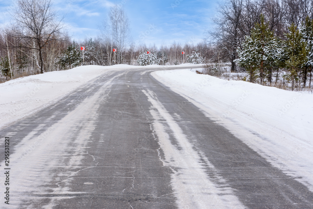 Patterns on the winter highway in the form of four straight lines. Snowy road on the background of snow-covered forest. Winter landscape. Patterns on the winter highway in the form of four straight lines. Snowy road on the background of snow-covered forest. Winter landscape.