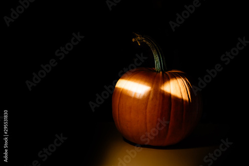 big orange pumpkin with luminous eyes on a black background illuminated by an artificial light source