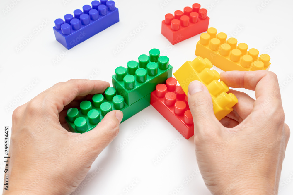 Hands constructing from colorful toy plastic bricks, blocks for building on white background Hands constructing from colorful toy plastic bricks, blocks for building on white background