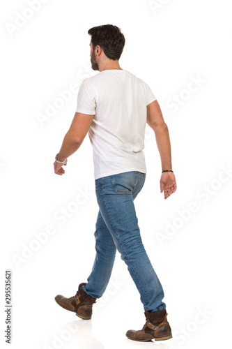 Young Man In Jeans And White T-shirt Is Walking. Rear Side View
