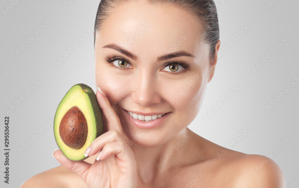 Beautiful smiling woman with clean skin holds ripe avocado near the face. Cosmetology skin care