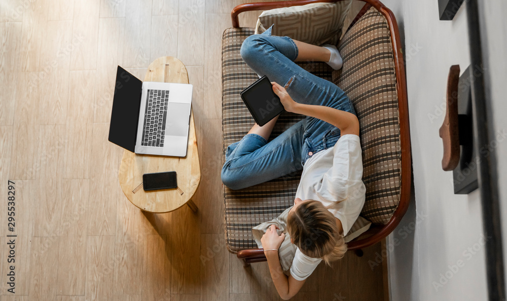Woman is laying on a sofa and using a e reader while resting from working with a laptop. Study and work online, freelance. Girl is working with her notebook laying on a couch. Woman is laying on a sofa and using a e reader while resting from working with a laptop. Study and work online, freelance. Girl is working with her notebook laying on a couch.