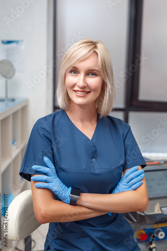 Cosmetology Service. Young doctor in gloves at beauty clinic standing crossed arms smiling confident