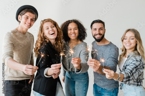 Row of young excited friends holding sparkling bengal lights in front of camera