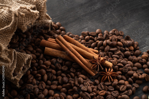 Coffee beans spill out of a bag with cinnamon sticks and star anise.
