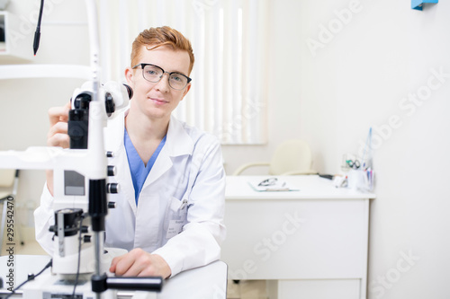 Young successful eye doctor in uniform testing new ophthalmological equipment