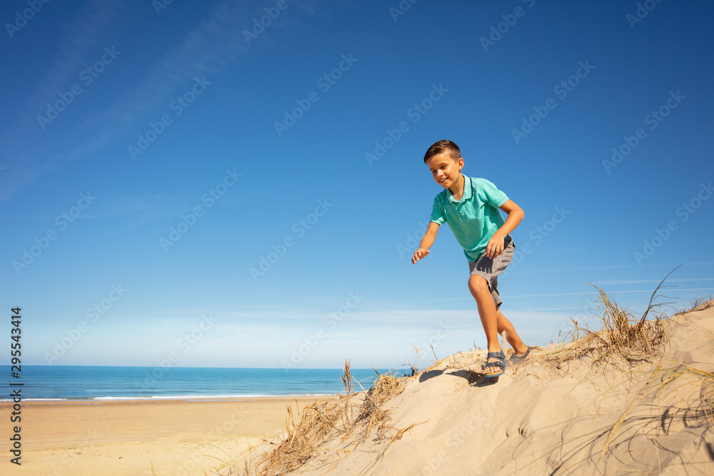 Happy handsome boy jump from sand dune near sea Happy handsome boy jump from sand dune near sea