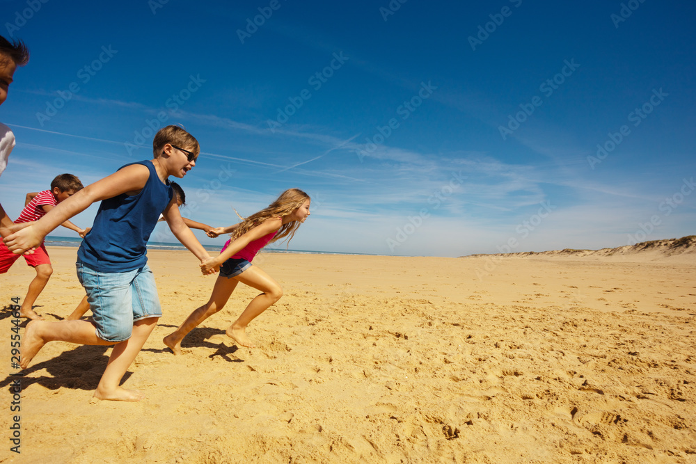 Group of kids run holding hands on the sea beach Group of kids run holding hands on the sea beach