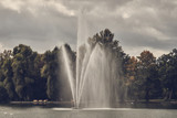 fountain in the lake against the background of an autumn forestand a lead cloudy sky