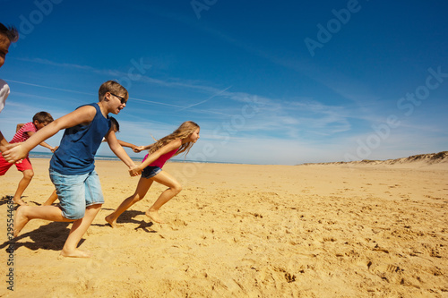 Group of kids run holding hands on the sea beach